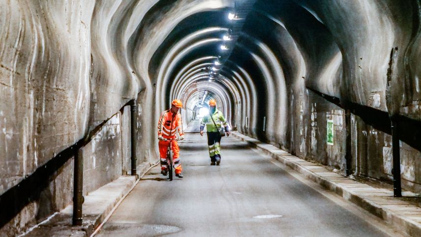 Bauarbeiter unterwegs im Tunnel Munt la Schera der Engadiner Kraftwerke AG. Gut zu erkennen sind die punktuellen Ausweitungen im Lichtraumprofil des Tunnels. 					Foto: Jon Duschletta