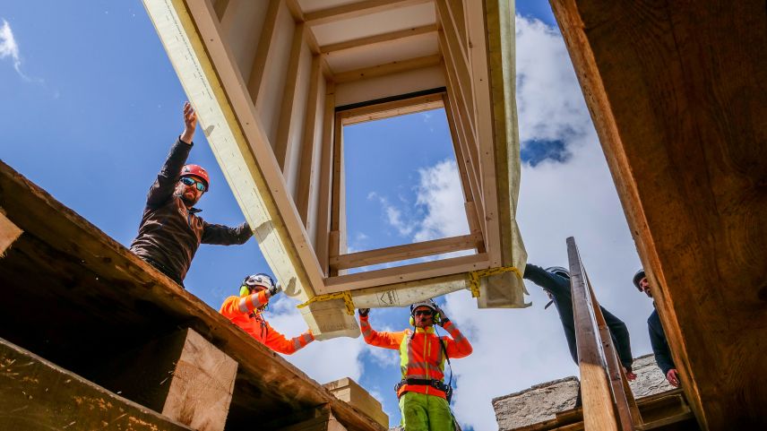 Flughelfer der Heli Bernina und Mitarbeiter der Holzbaufirma Nusser manövrieren das «heranschwebende» Element des neuen Dachausstiegs punktgenau auf die vorbereitete Dachöffnung. Foto: Jon Duschletta
