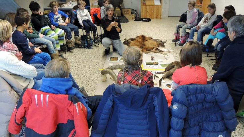 Ils uffants cun lur magistras taidlan cun attenziun als pleds dad Anna Mathis (fotografia: Benedict Stecher).