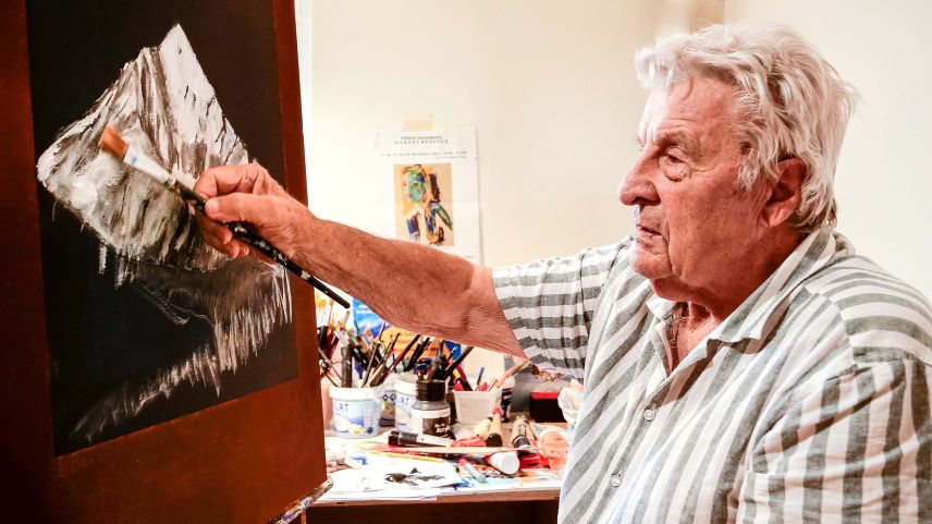 Hubert Bezzola, poliglot e cosmopolit, in seis atelier a Zernez cun ün purtret dal Piz Linard (fotografia: Jon Duschletta).