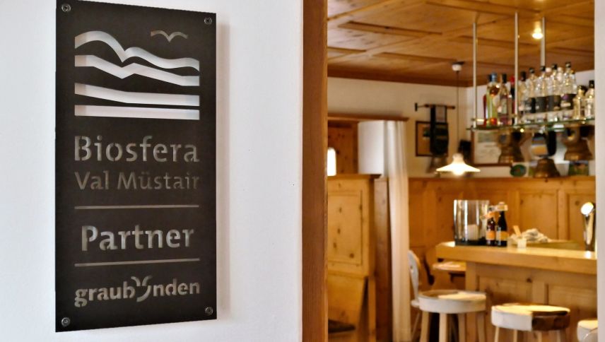 La tabla chi simbolisescha il partenadi culla Biosfera – in quist cas a l’entrada da l’ustaria i’l Hotel Central a Valchava (fotografia: Parc da natüra Biosfera Val Müstair).