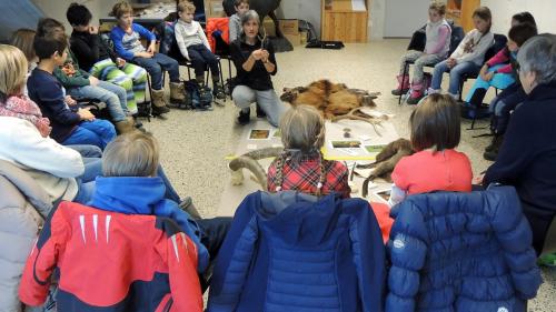 Ils uffants cun lur magistras taidlan cun attenziun als pleds dad Anna Mathis (fotografia: Benedict Stecher).