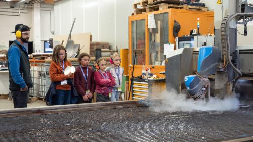 Jon-Corsin Neuhäusler (links) der Tschenett AG beobachtet mit MINT-Schülerinnen gespannt, wie ein Wasserstrahl die zuvor programmierten Dachteile ihres Vogelhäuschens aus einer Aluminiumplatte schneidet. Fotos: Jon Duschletta